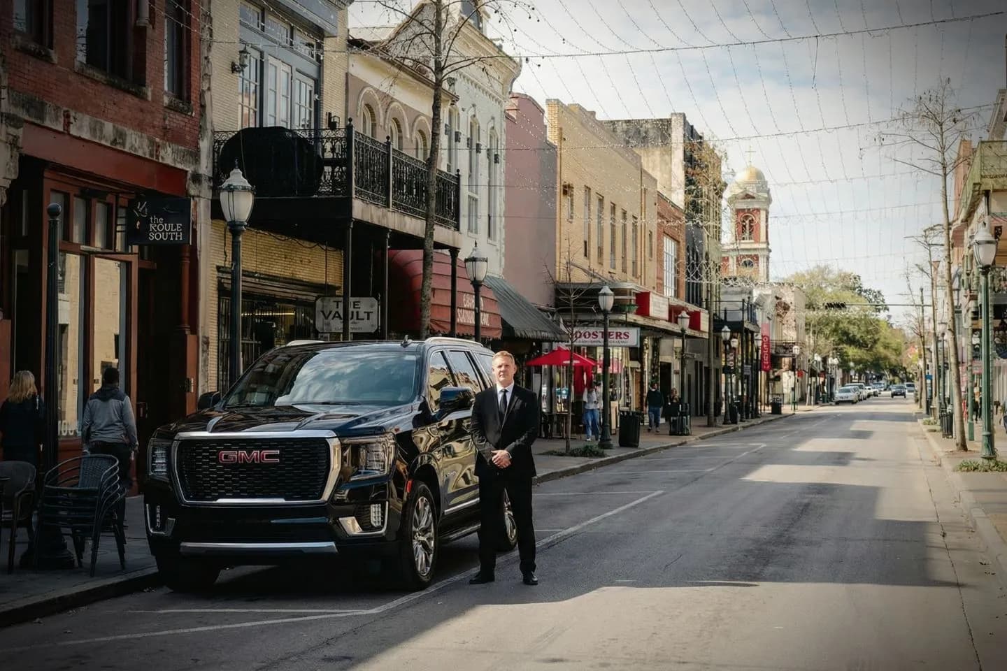 Luxury black sedan with Alabama, AL Chauffeur Service driver assisting passenger outside airport terminal