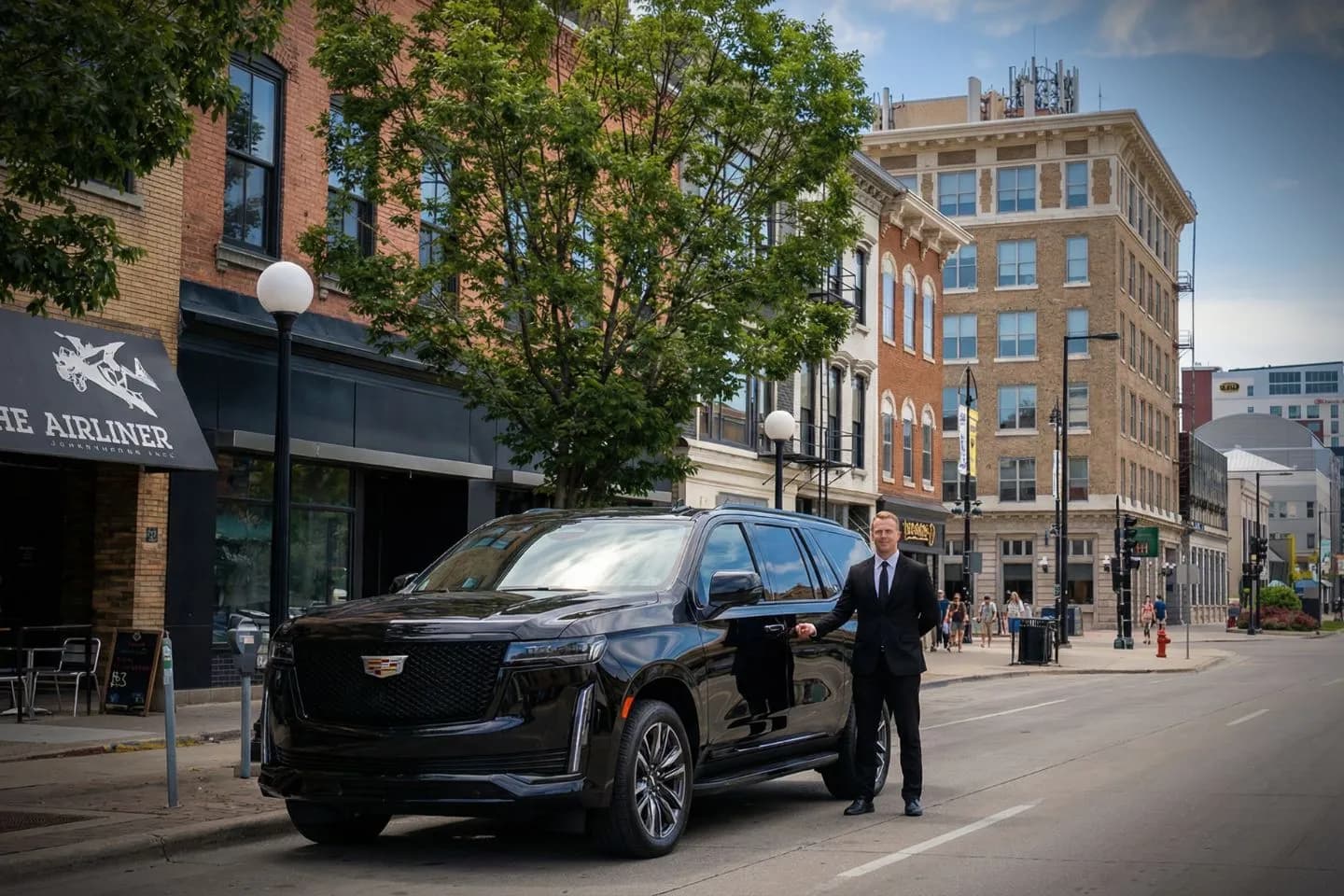 Executive Iowa chauffeur service vehicle with chauffeur assisting client in downtown Iowa business district