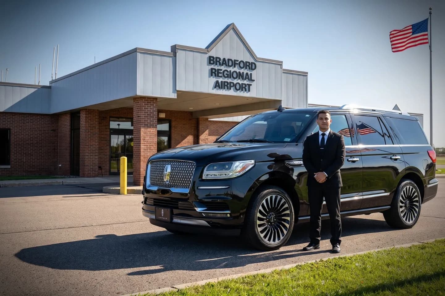 Chauffeur in a dark suit standing beside a sedan at Bradford Regional Airport