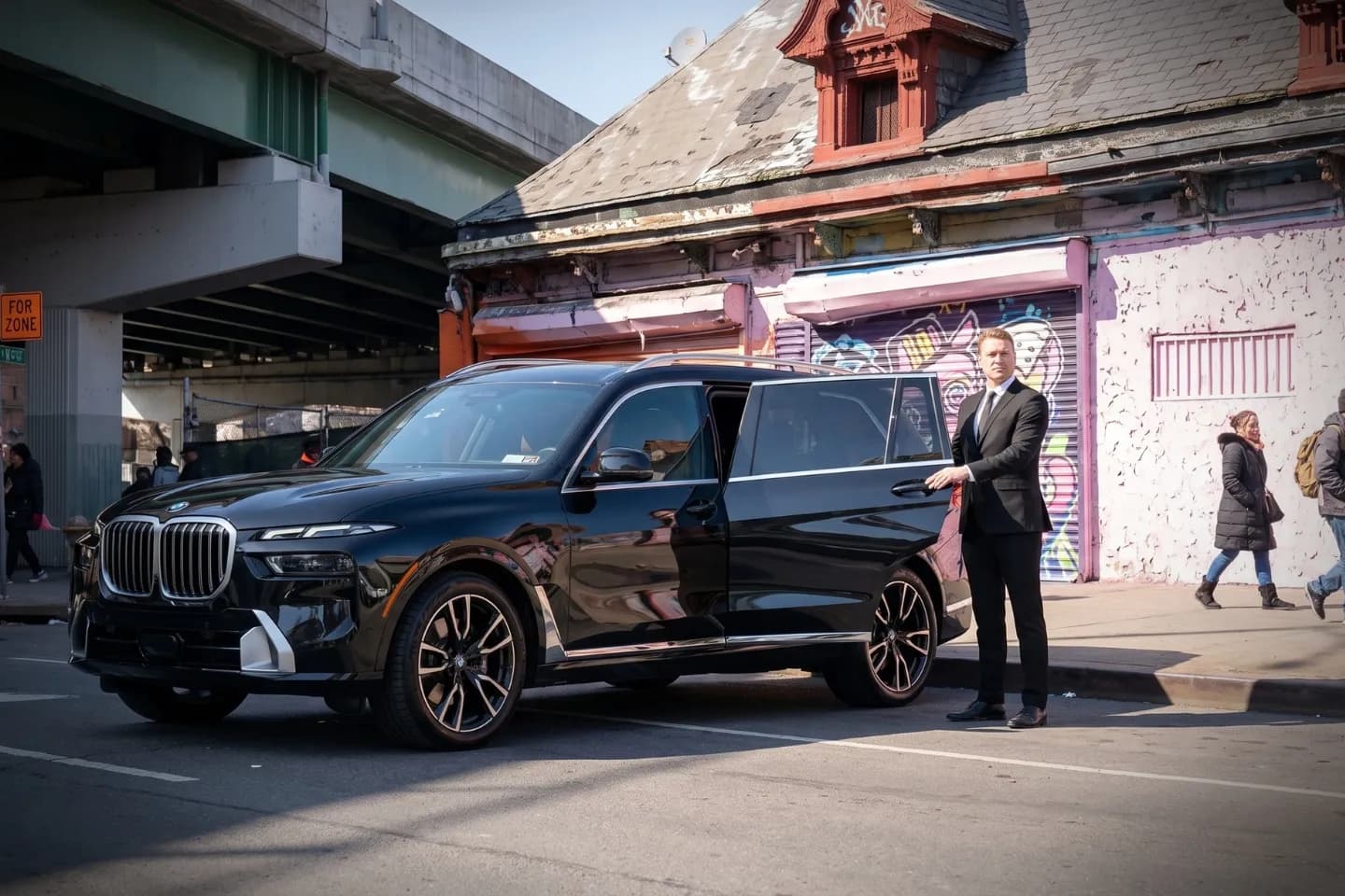 Uniformed driver standing beside a polished black car in Hunts Point, Bronx